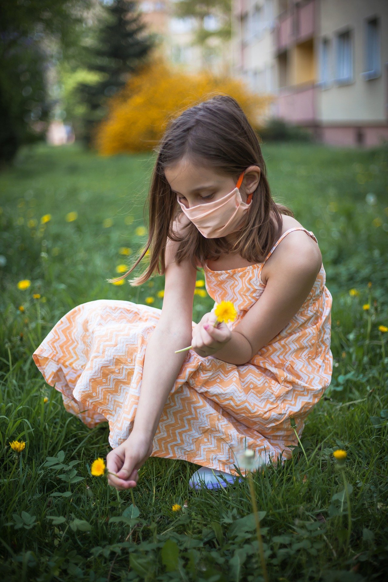 Girl during COVID-19 playing in the grass picking flowers. 