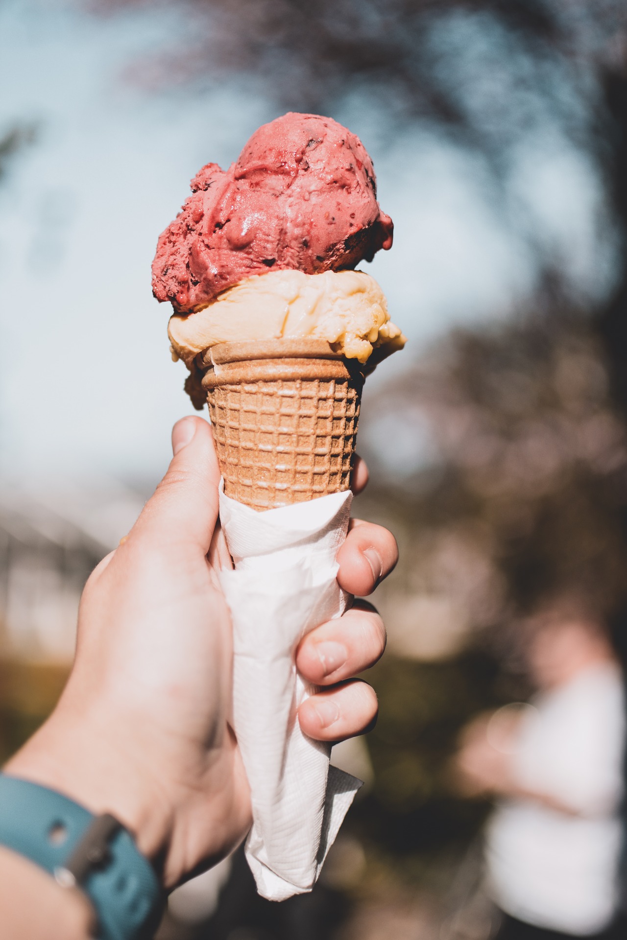 Ice cream cone in students hand with strawberry and vanilla scoops. 